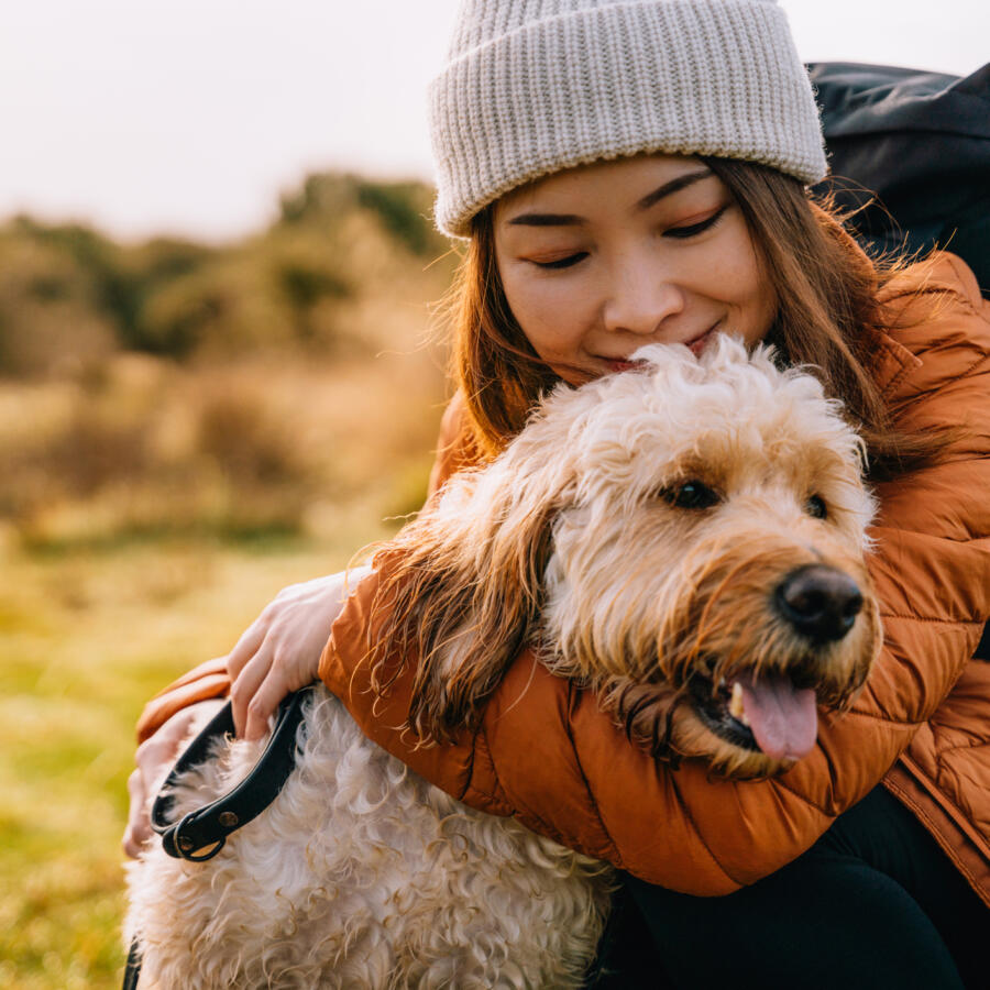 Young Asian woman hugging her dog while hiking in autumn nature.