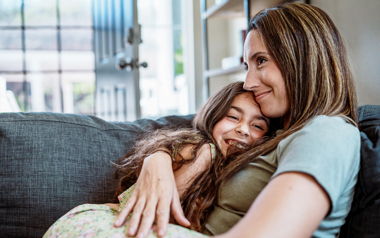 Young girl and mother hug each other on the couch